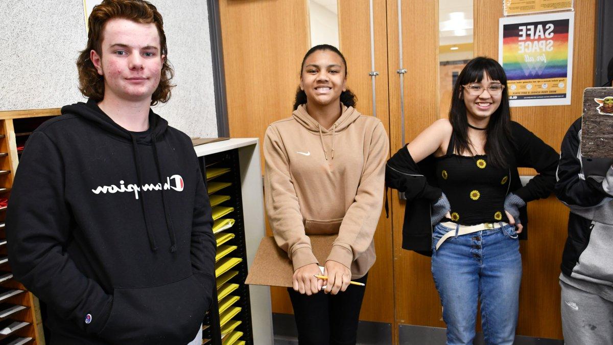 three students standing by a door and smiling